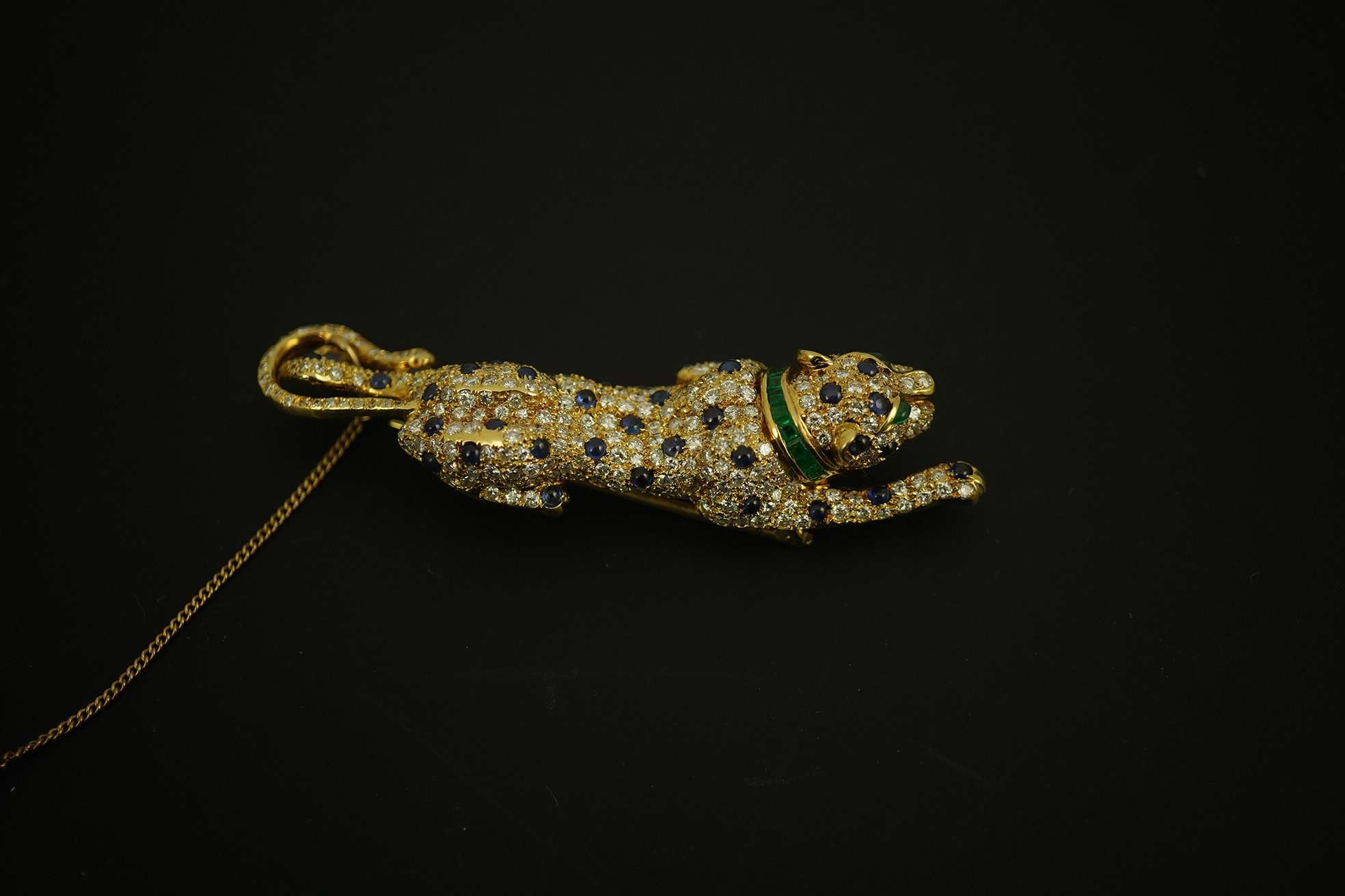 A modern Cartier style 18k gold, sapphire, emerald and diamond cluster set stalking panther brooch